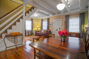 A spacious living room with a wooden dining table, a brown leather sofa, and a staircase with white railings.