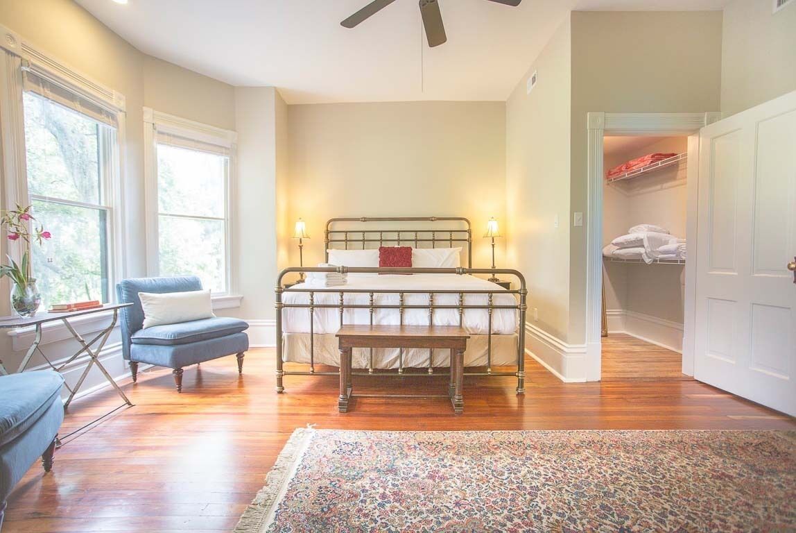 A bedroom with a metal bed frame, a wooden bench, a blue armchair, and a patterned rug.