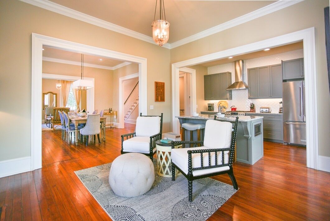 Un salon spacieux doté d’un parquet, d’un grand pouf rond et d’un coin repas agrémenté d’un lustre.