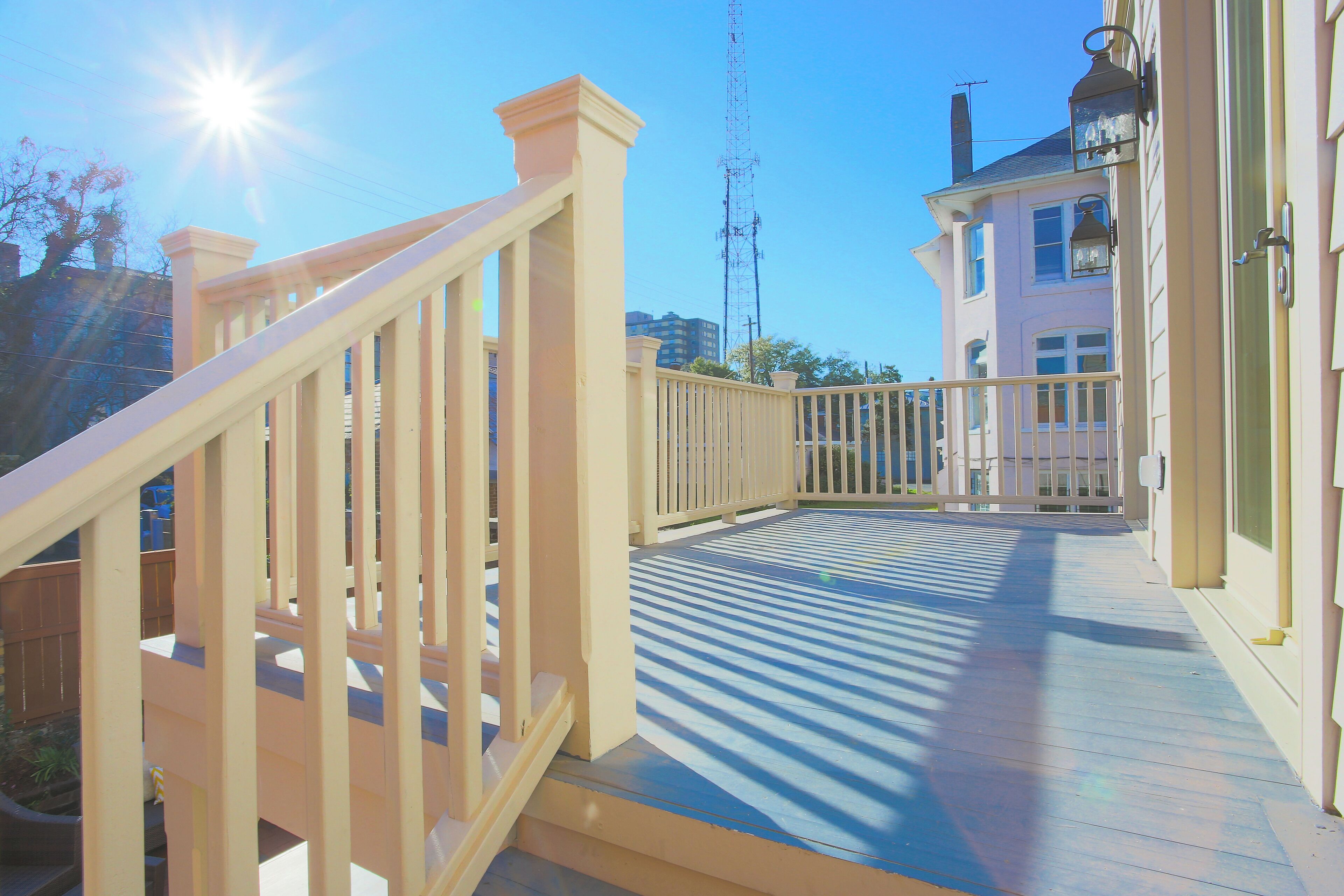 A wooden deck with a railing, leading to a building with a white facade and a chimney.