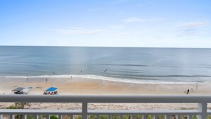A beach with a clear view of the ocean, a few people, and beach umbrellas. - Luxury, direct oceanfront 2/2, top-floor corner with wrap-around balcony and heated pool (New Smyrna Beach)