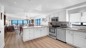 A modern kitchen with white cabinets, a large island, and a view to the outside. - Luxury, direct oceanfront 2/2, top-floor corner with wrap-around balcony and heated pool (New Smyrna Beach)