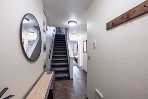 Un couloir avec un banc en bois, un miroir et un escalier menant à une autre pièce.
