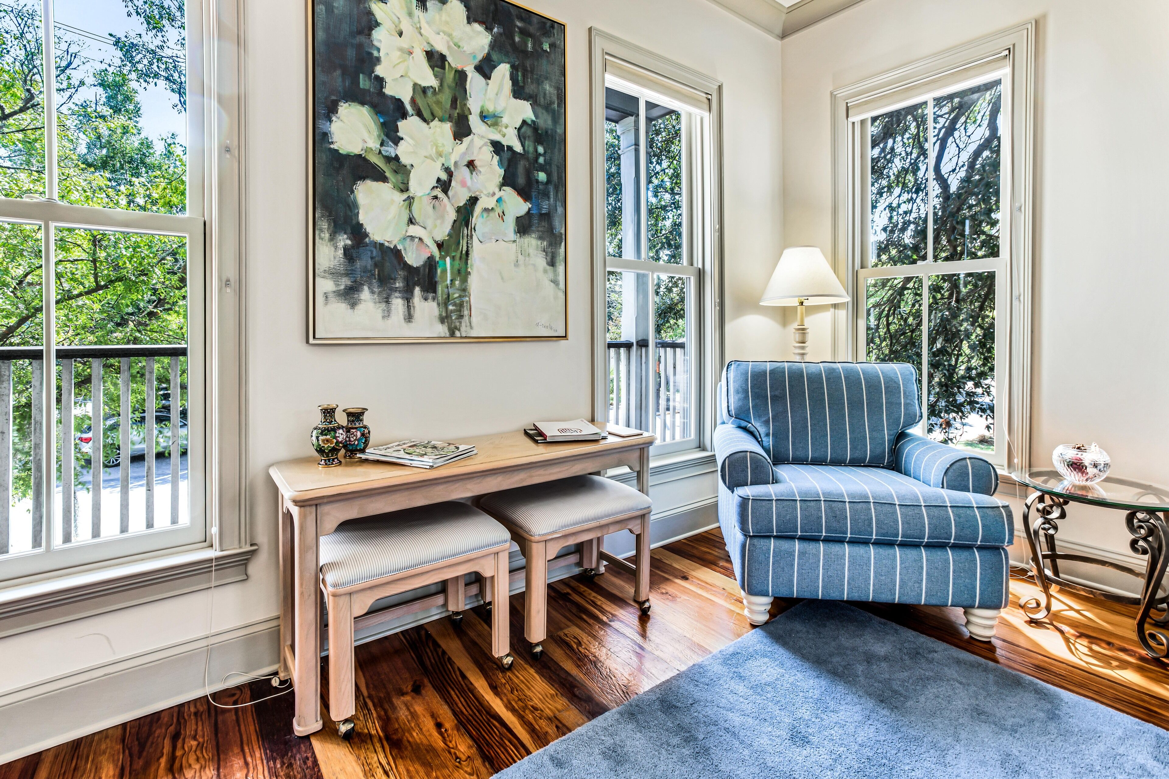 Een kamer met een houten bureau, een blauwe fauteuil en een groot schilderij van bloemen aan de muur.