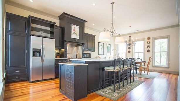 A modern kitchen with dark cabinetry, a stainless steel refrigerator, and a central island with bar stools.