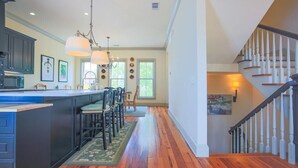 A spacious kitchen with a central island, wooden flooring, and a staircase with white balusters.