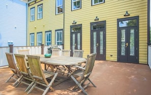 A patio with a round wooden table and chairs, a grill, and a yellow building with black doors.