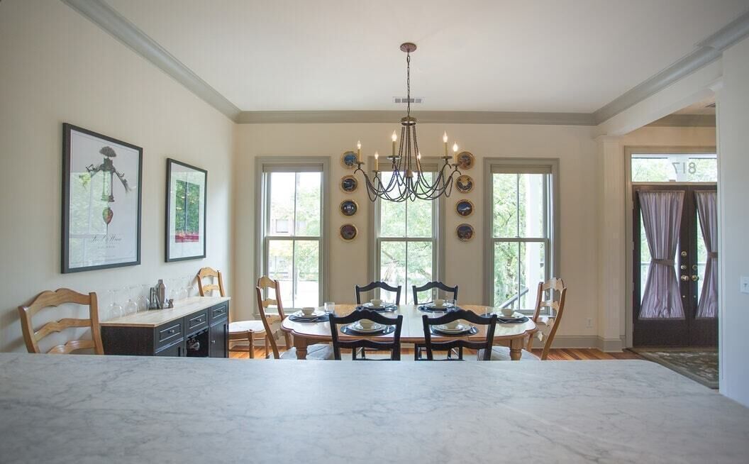 A dining room with a marble table, wooden chairs, a chandelier, and large windows.