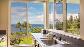 A kitchen with a large window offering a view of the ocean and palm trees.