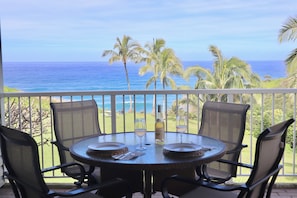 A round table with four chairs on a balcony overlooking the ocean.