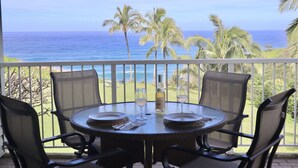 A round table with four chairs on a balcony overlooking the ocean.