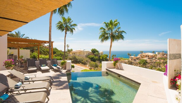 Un espace piscine avec des chaises longues, une pergola et une vue sur l’océan.