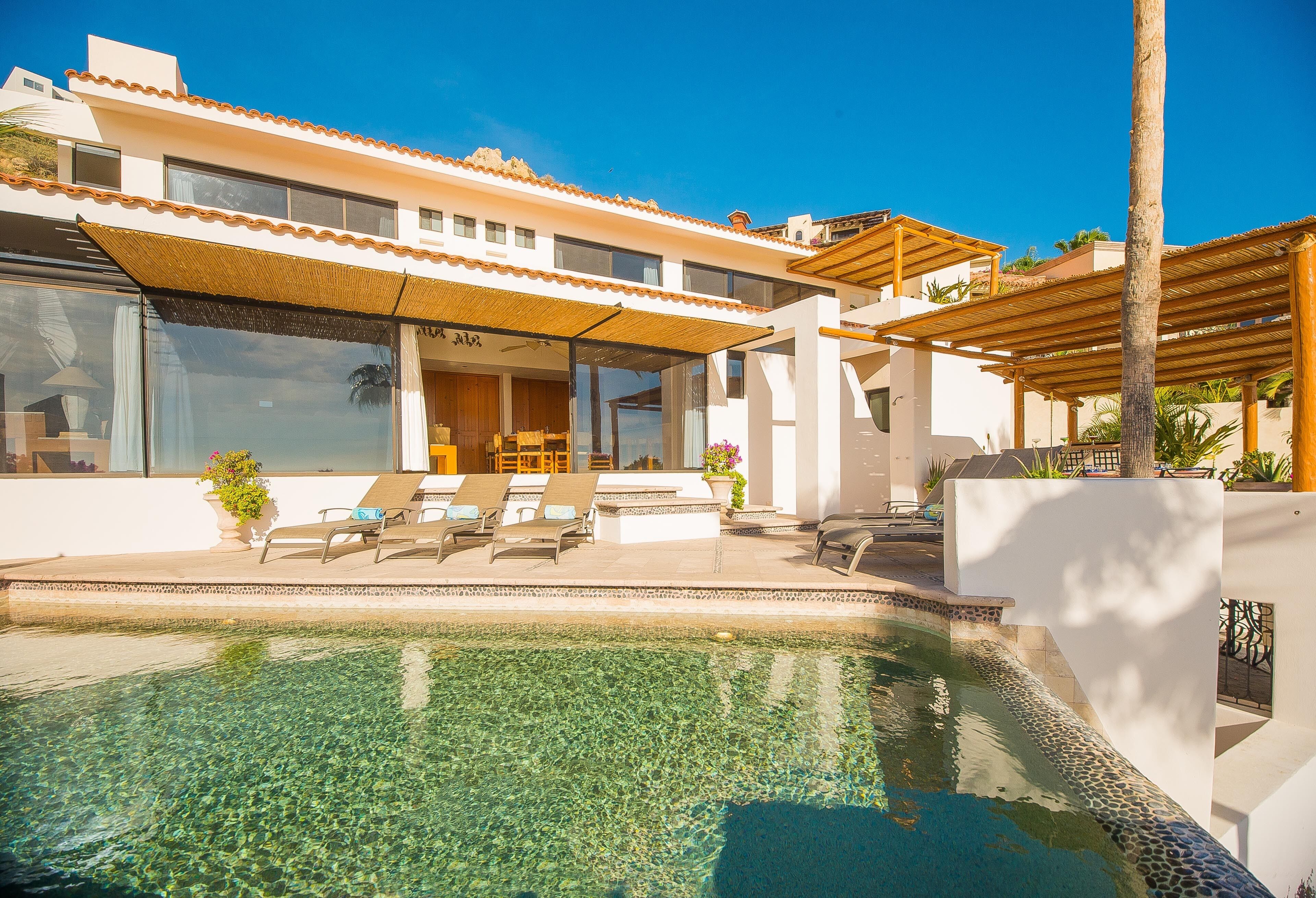 A modern house with a swimming pool, sun loungers, and a covered patio area.