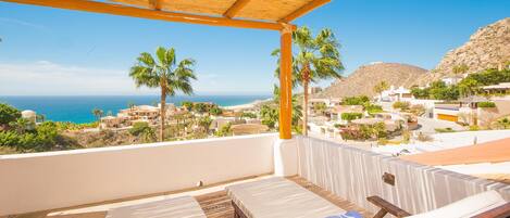 A balcony with a view of the sea and a hillside.