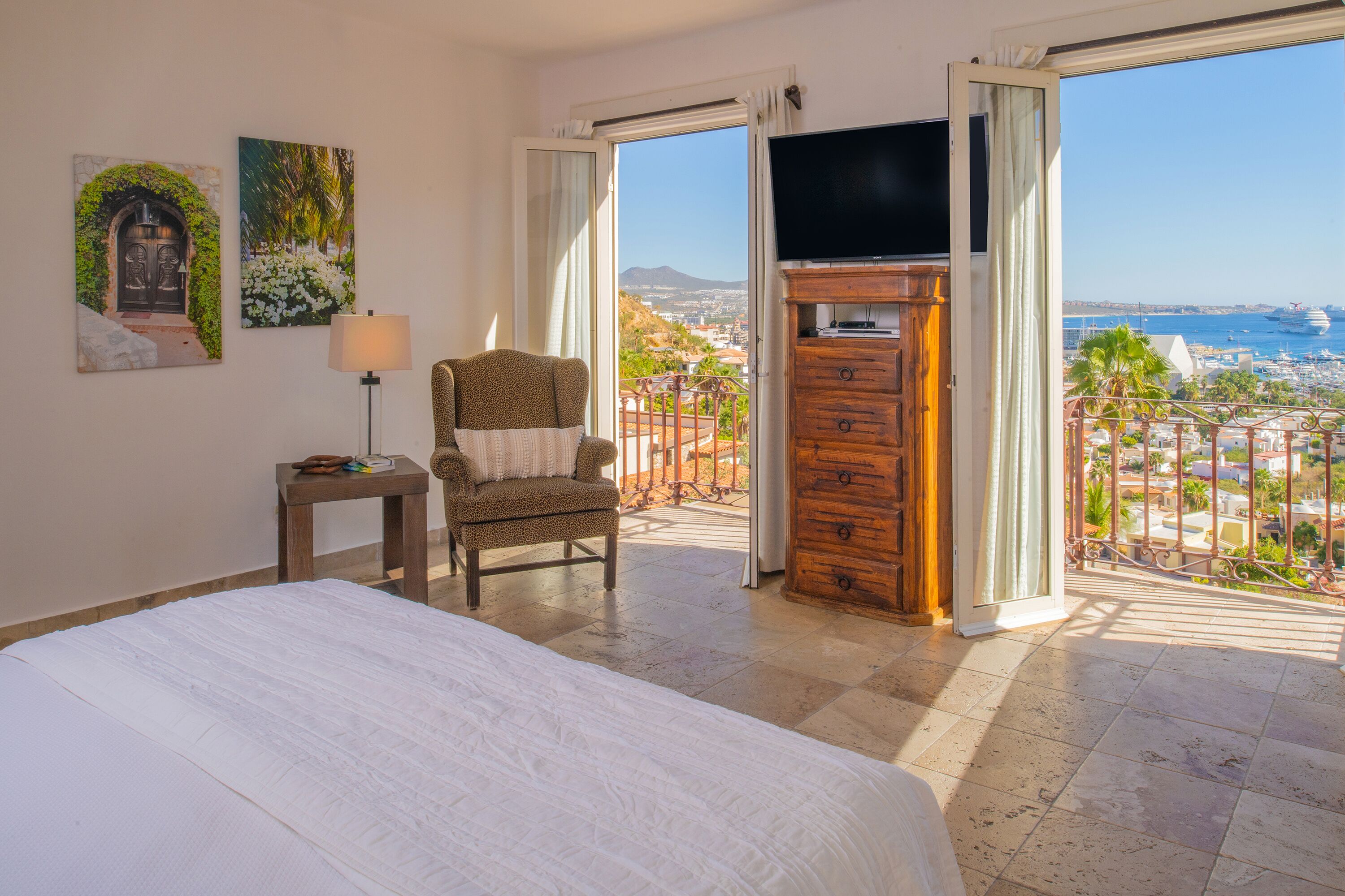 A hotel room with a bed, a chair, a TV, and a balcony with a view of the sea.