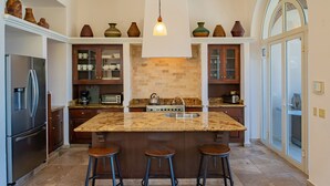 A kitchen with a marble island, stools, a stove, and cabinets. - Pedregal Walk to Beach/Town Villa w/ Ocean, Bay & Marina Views, Pool & Hot Tub (Cabo San Lucas)
