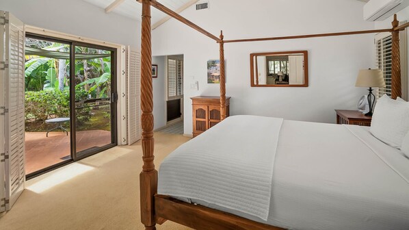 Una cama con dosel en una habitación con puerta corrediza de vidrio que da a un patio con vegetación.