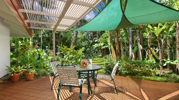 Un patio con mesa y sillas, rodeado de abundante follaje y una estructura de pérgola.