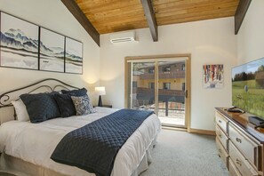 Quarto com cama, TV e varanda com vista para um prédio.