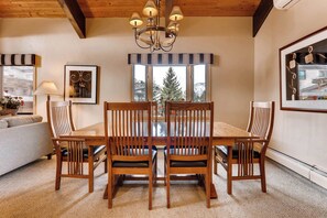 Uma área de refeições com mesa e cadeiras de madeira, um candelabro e vista para uma montanha nevada pela janela.