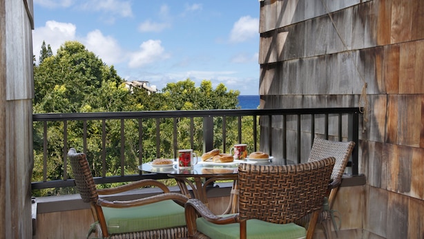 Un balcon avec des fauteuils en osier et une table où sont disposées des pâtisseries et une boisson.