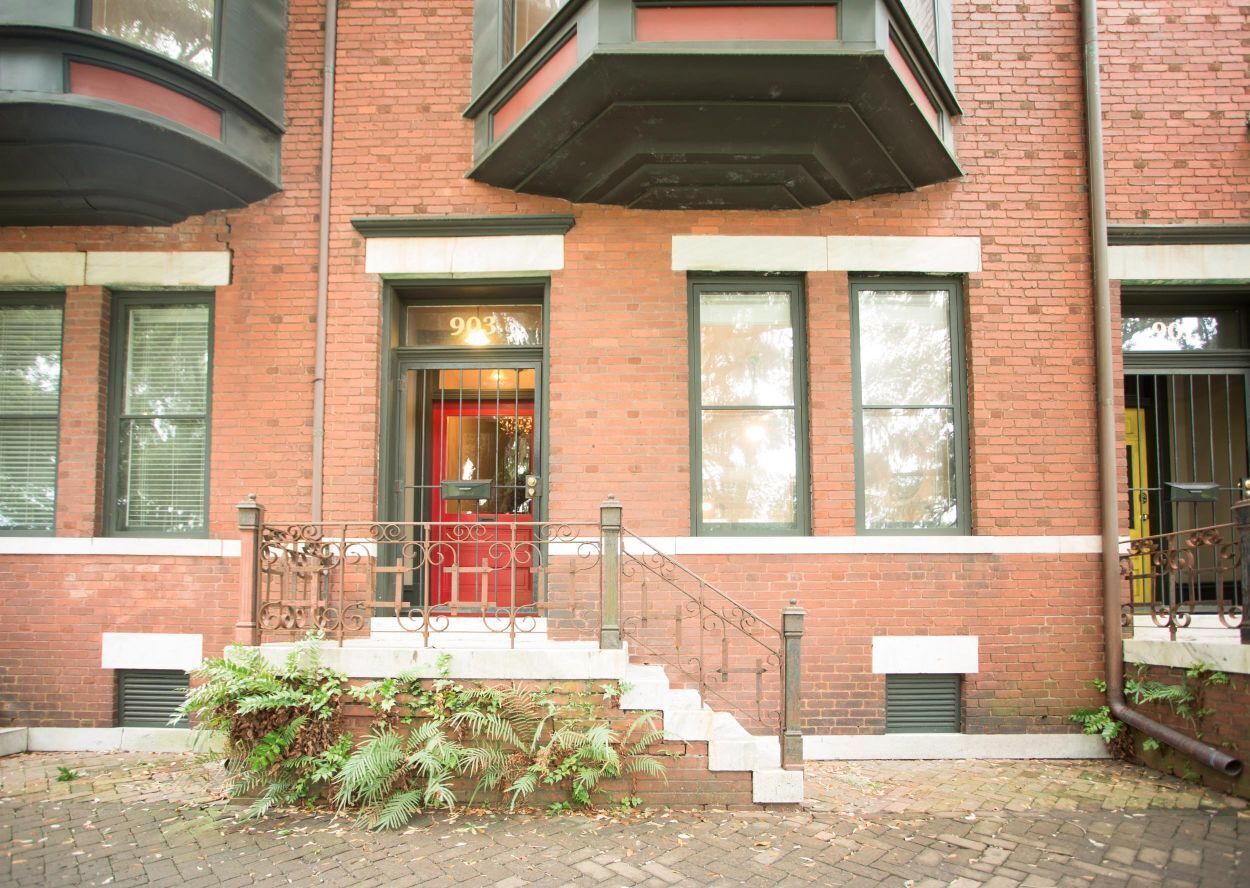 A brick building with a red door, a small porch, and a staircase leading to the entrance.