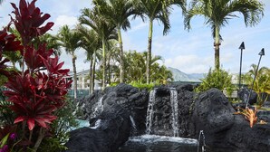 A tropical resort with a waterfall, palm trees, and a pool. - Ocean and Mountain Views - Spacious Cliffs 5-301 .. 1 BR plus Loft (Princeville)
