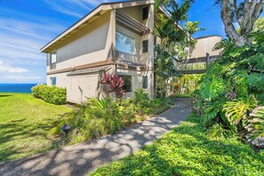 A two-story house with a garage, surrounded by lush greenery and a view of the ocean. - Pali Ke Kua 121 offer Stunning Oceanfront Views (Princeville)
