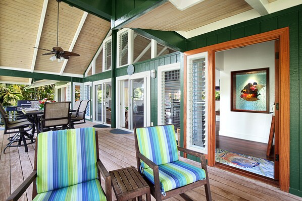 A covered outdoor area with wooden furniture, including chairs and a table, and a door leading to an interior space.
