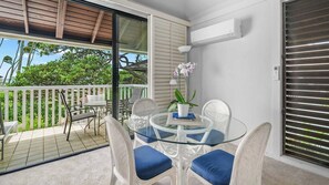 A balcony with a glass table and wicker chairs, a potted orchid, and a view of greenery.