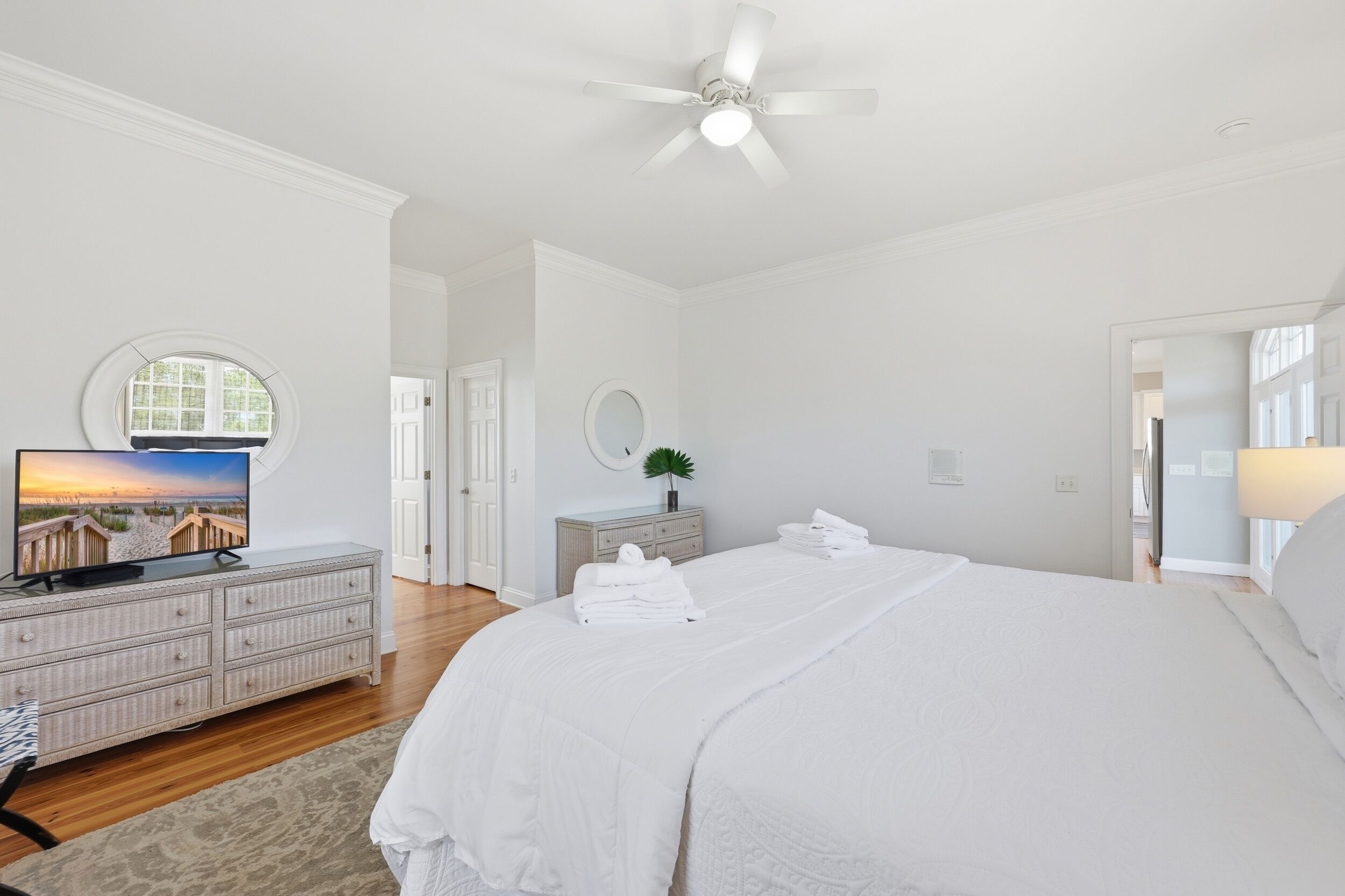 Un dormitorio con cama, televisión, cómoda, espejo y ventilador de techo.