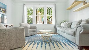 A living room with a sofa, armchair, and a small table. There is a window with a view of greenery and a building. - First Floor Condo w/ Large Living Area in Historic Dist. by Lucky Savannah (Savannah)