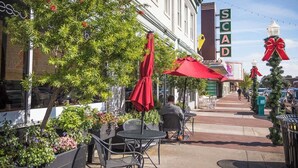 An outdoor café with tables and chairs, a street with a sign reading "SCAD", and a Christmas tree with a red bow. - First Floor Condo w/ Large Living Area in Historic Dist. by Lucky Savannah (Savannah)