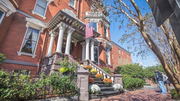 A red brick building with a grand entrance, a flag, and a staircase with flowers. - First Floor Condo w/ Large Living Area in Historic Dist. by Lucky Savannah (Savannah)