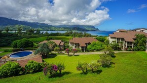 A resort with multiple buildings, a swimming pool, and a view of the ocean and mountains. - Aloha Condos, Hanalei Bay Resort, Condo 6303, Ocean View, AC (Princeville)