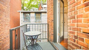 Ein kleiner Balkon mit einem Metalltisch und -stühlen, Backsteinwänden und einer zur Wohnung hinweisenden Tür.