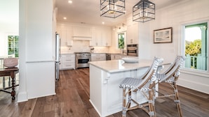 A modern kitchen with white cabinetry, a large island, and two wicker bar stools.