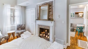 Une chambre à coucher avec un grand lit, une cheminée, un miroir et une vue sur une autre pièce.