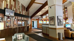 Eine Lobby mit Bar und Grill namens 'Altitude', Wandverkleidung aus Holzpaneelen, einem Empfangstresen und einer Sitzecke mit einer Couch und Sesseln.