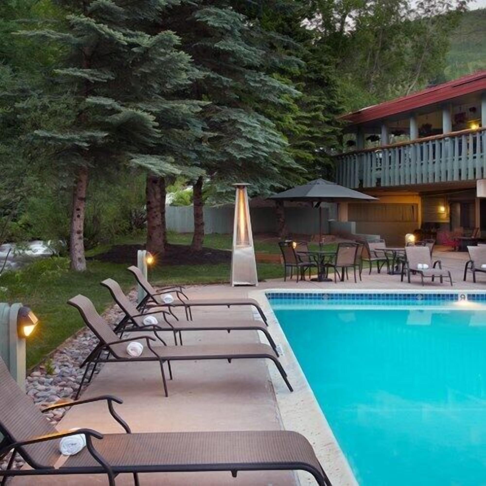 A pool area with lounge chairs, a table, and a building with a balcony.