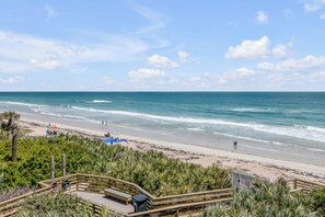 Une vue sur la plage avec une terrasse en bois, des palmiers et un ciel dégagé.