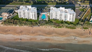 Un hôtel en bord de mer, avec plusieurs étages, une piscine et une plage en premier plan.