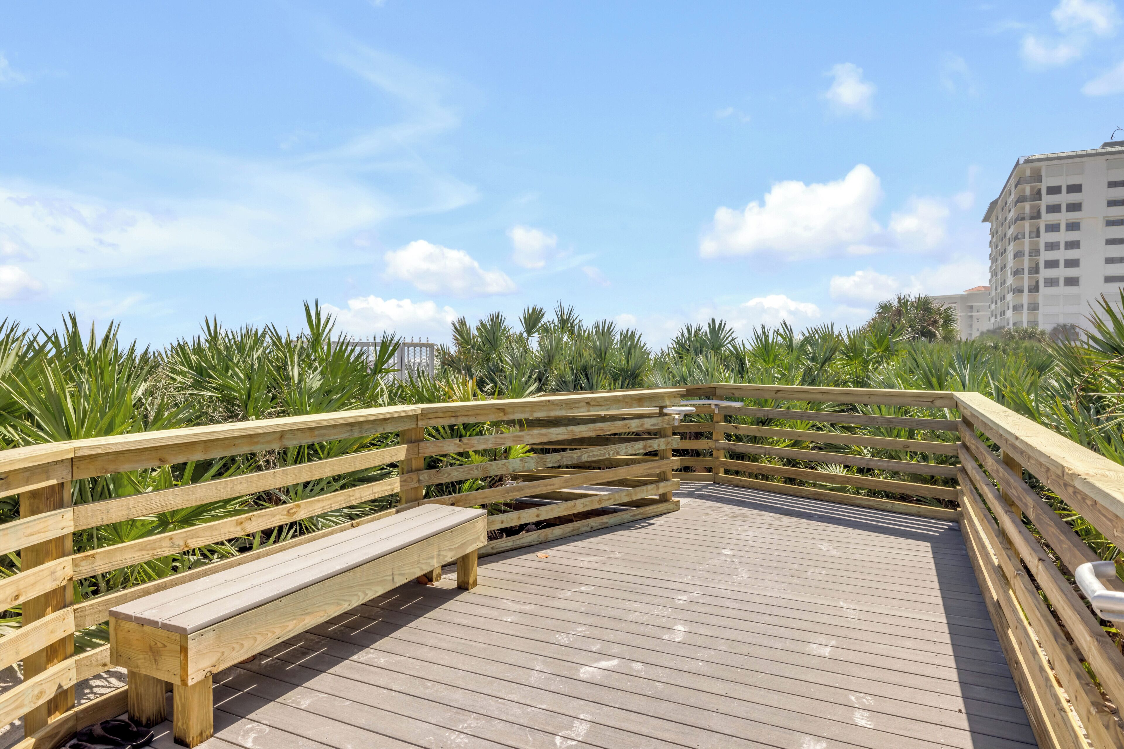 Un muelle de madera con bancos, rodeado de vegetación y edificios al fondo.