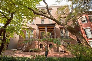 A brick building with a central staircase, arched windows, and a tree in the foreground.