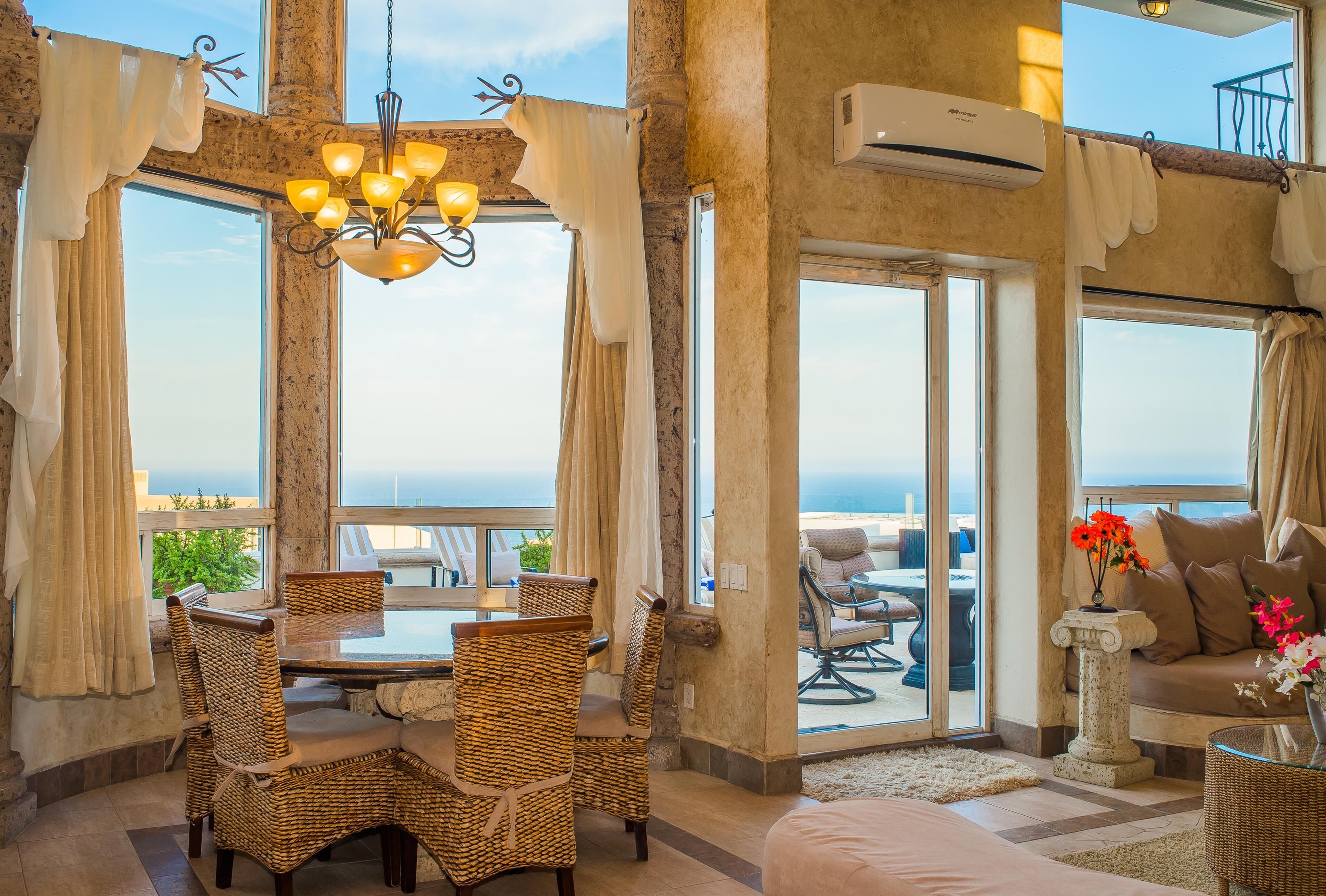 A spacious room with a balcony, wicker furniture, a chandelier, and a view of the sea.