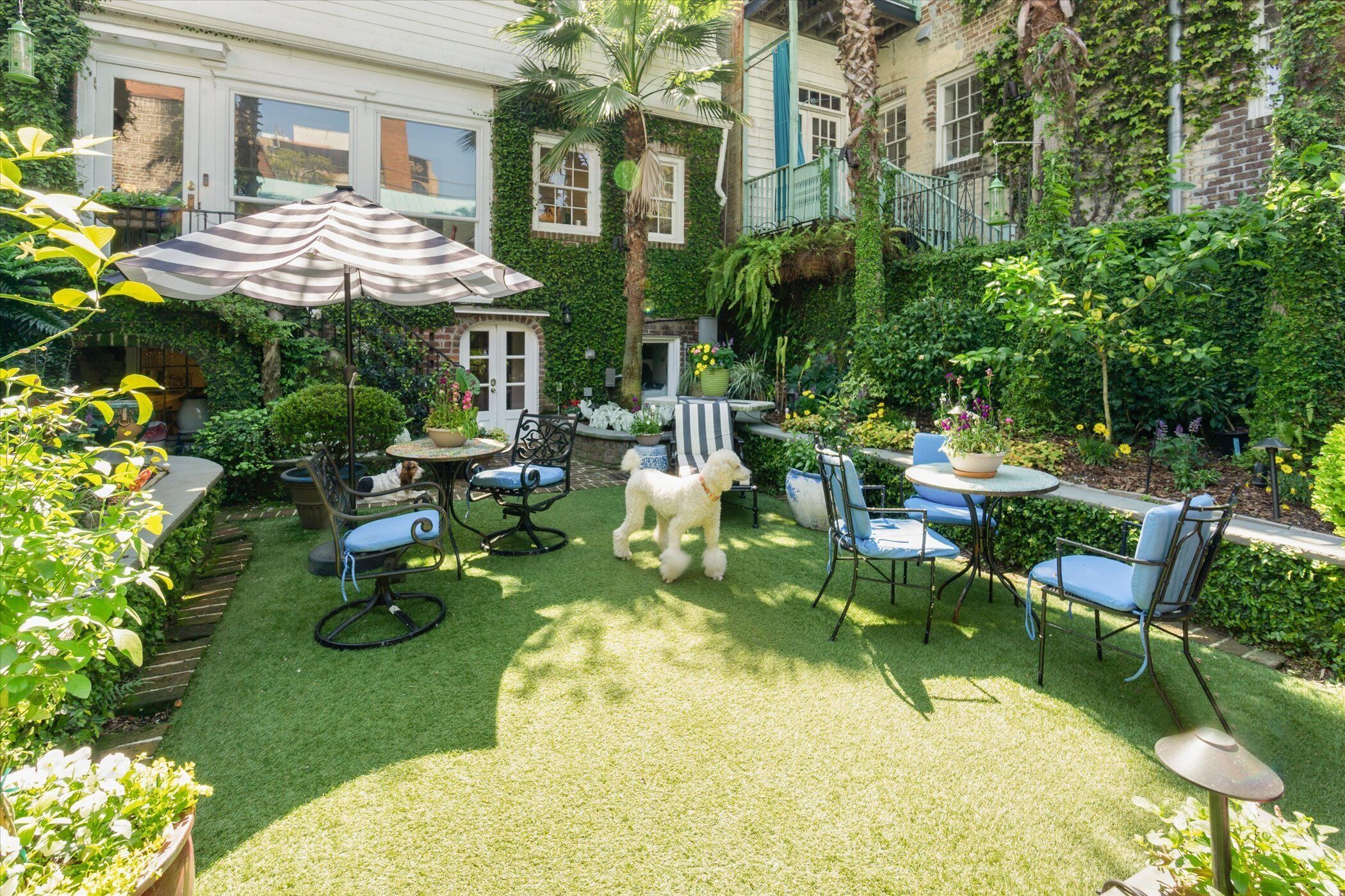 A well-maintained patio with a small dog, outdoor furniture, and lush greenery.