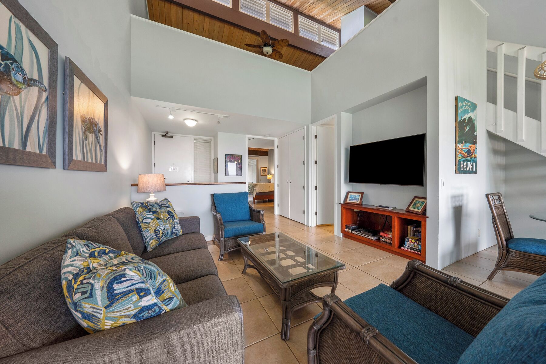 A spacious living room with a high ceiling, a television mounted on the wall, and a staircase leading to an upper level.