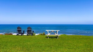 A grassy area with two Adirondack chairs and a picnic table by the ocean. - Majestic Ocean View Top Floor Getaway Cliffs 7305 (Princeville)