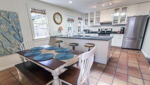 A kitchen with a dining area, white cabinets, a stainless steel refrigerator, and a clock on the wall.