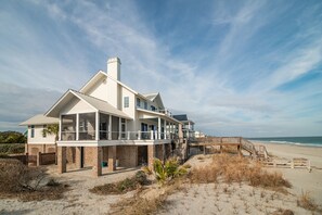 Una casa frente al mar con un balcón grande, una terraza de madera y vistas al océano.